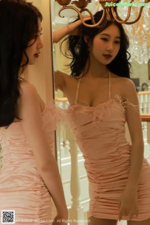 A woman in a pink dress leaning against a wall.