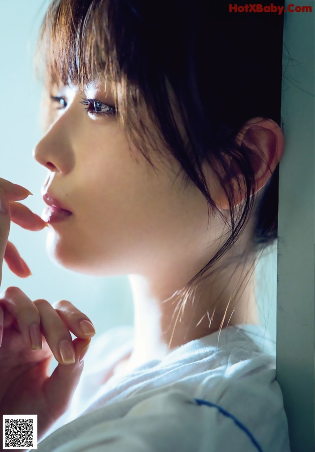 A woman in a white shirt is looking out a window.