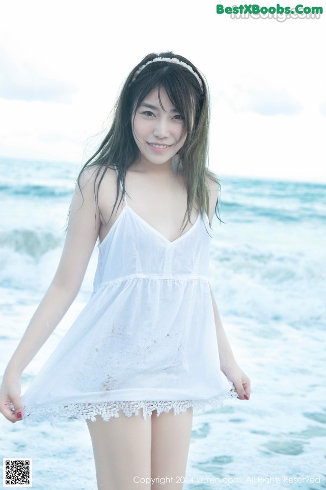 A woman in a white dress standing on the beach.