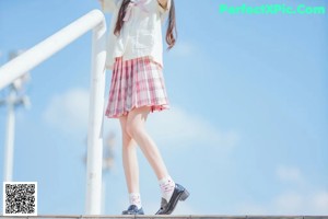 A woman in a white shirt and pink plaid skirt holding a yellow hat.
