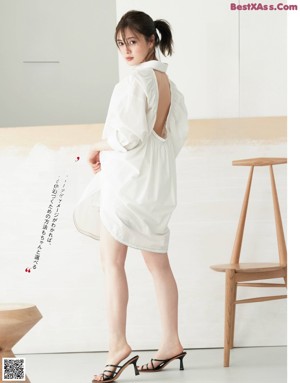 A woman in a white dress standing in front of a white wall.