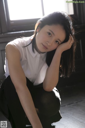 A woman with long black hair standing in front of a wall.