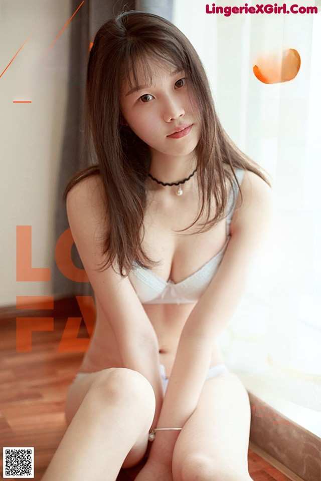 A woman sitting on the floor in a white bra and panties.