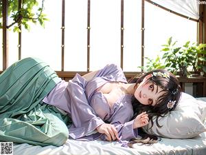 A woman in a blue kimono sitting on a stone wall next to a pond.