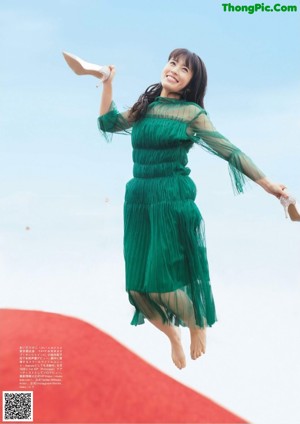 A woman in a green dress sitting on a window sill.